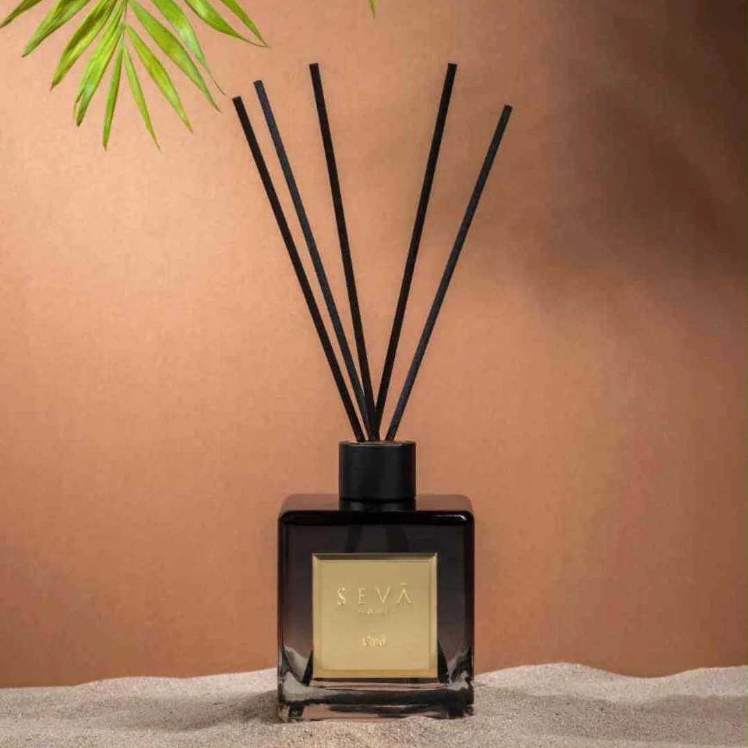 Black glass reed diffuser with black reeds against a warm wall